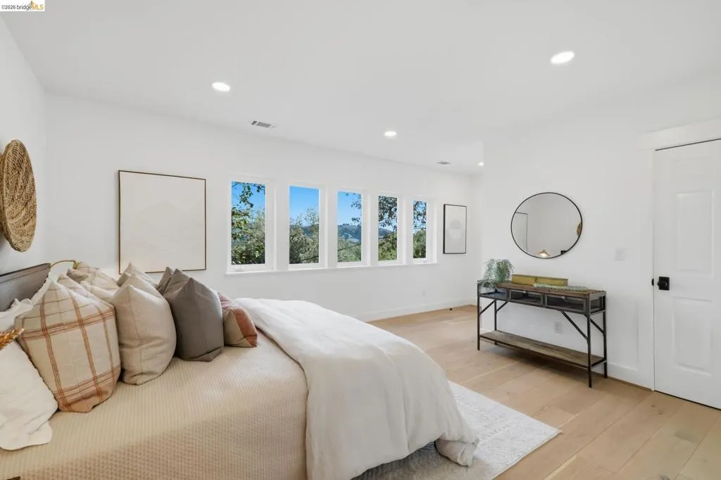 Recessed lighting, light-toned wood-finish flooring, white walls, multiple windows, and a white paneled door with black hardware Recessed lighting, light-toned wood-finish flooring, white walls, multiple windows, and a white paneled door with black hardware