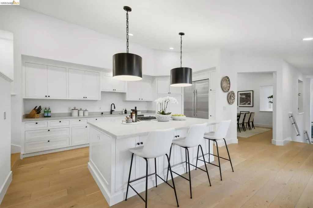 Light wood-finish flooring, white cabinetry, quartz countertops, stainless steel appliances, and a central island with pendant lighting Light wood-finish flooring, white cabinetry, quartz countertops, stainless steel appliances, and a central island with pendant lighting