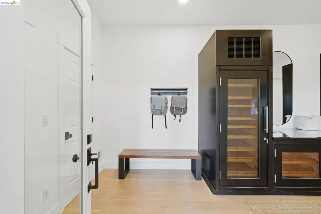 Wood-finish flooring, built-in wine refrigerator, white paneled door, black hardware, and a wood bench Wood-finish flooring, built-in wine refrigerator, white paneled door, black hardware, and a wood bench