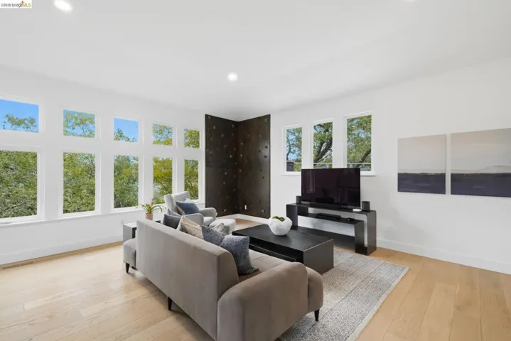 Expansive living area with light wood-finish flooring, a full wall of windows, recessed lighting, and a dark accent wall