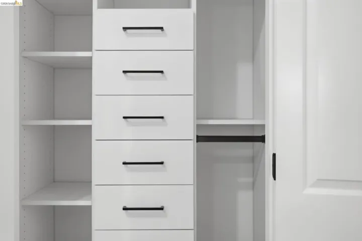 Built-in white cabinetry featuring multiple adjustable shelves, six drawers with matte black hardware, and an integrated hanging rod