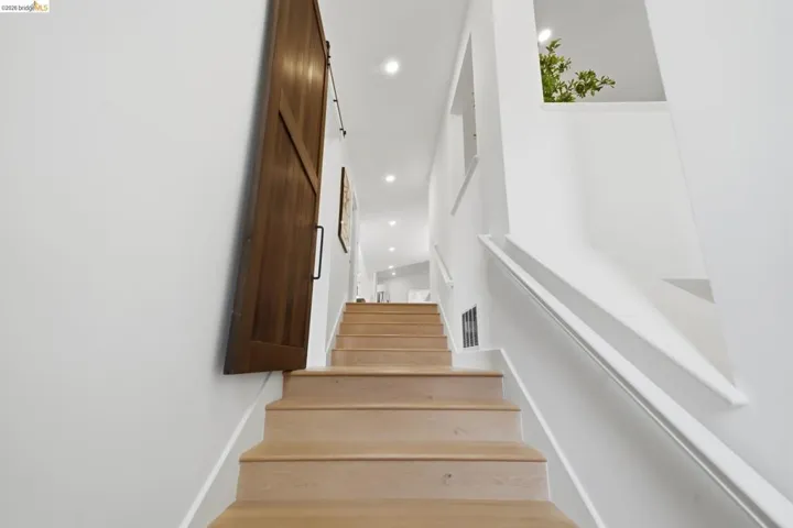 Wood-finish staircase with white risers, white wall-mounted handrail, and integrated ceiling lighting