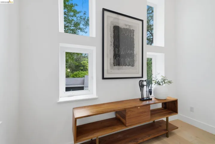 Multiple windows with white trim, wood-finish flooring, and a built-in wood console with open shelving