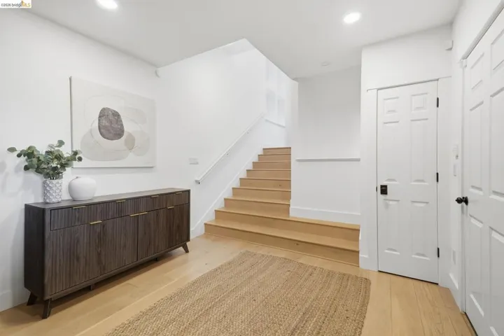 Wood-finish flooring throughout, white walls, and a staircase with natural wood treads