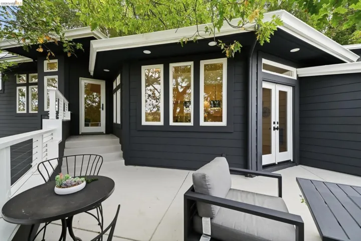 Exterior featuring dark siding, multiple large windows, a white cable railing, a concrete patio, and a white entry door