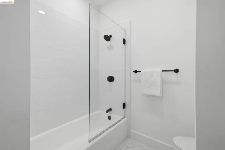Bathtub with white subway tile surround, clear glass shower panel, matte black fixtures, and hexagonal floor tiles