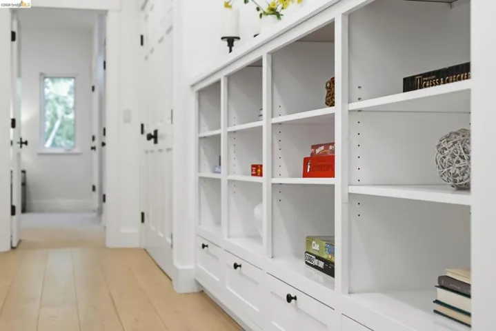 Built-in white shelving with adjustable shelves and integrated drawers, light wood-finish flooring, and white paneled doors with matte black hardware