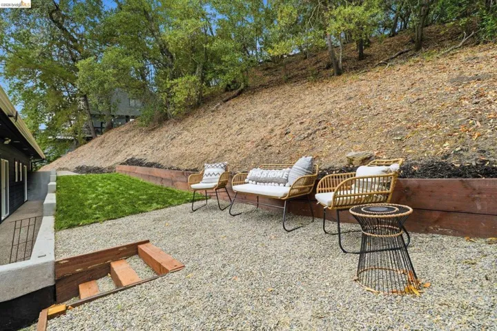 Gravel patio area with wood retaining walls, a section of manicured lawn, and mature trees in the background