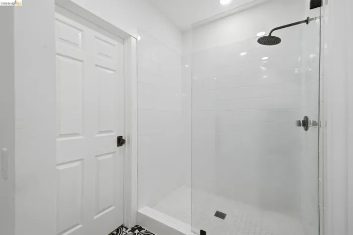 Enclosed shower with a glass panel, subway tile surround, hexagon tile flooring, and a matte black rain shower head