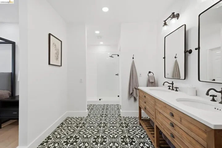 Dual vanity with wood-finish cabinetry and white countertop, black and white patterned floor tiling, and a glass-enclosed shower