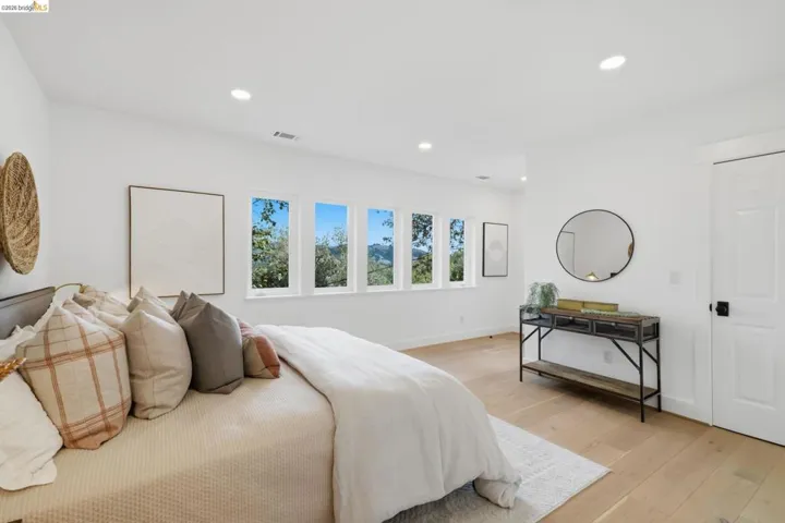 Recessed lighting, light-toned wood-finish flooring, white walls, multiple windows, and a white paneled door with black hardware