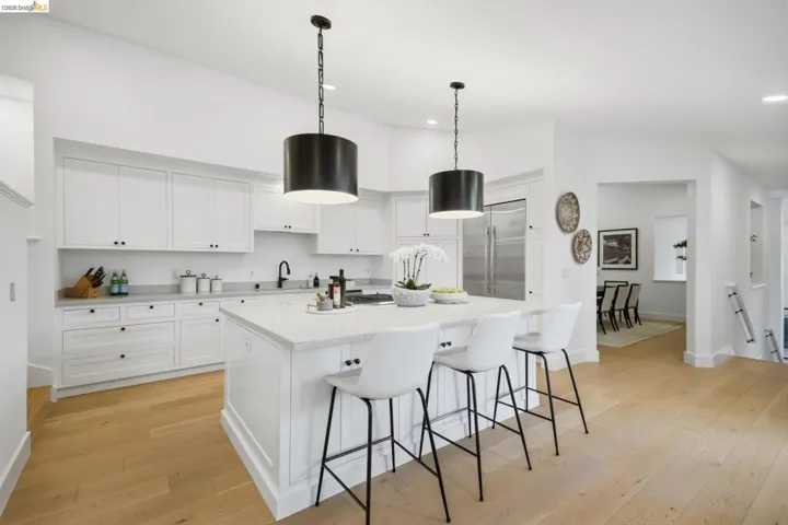 Light wood-finish flooring, white cabinetry, quartz countertops, stainless steel appliances, and a central island with pendant lighting