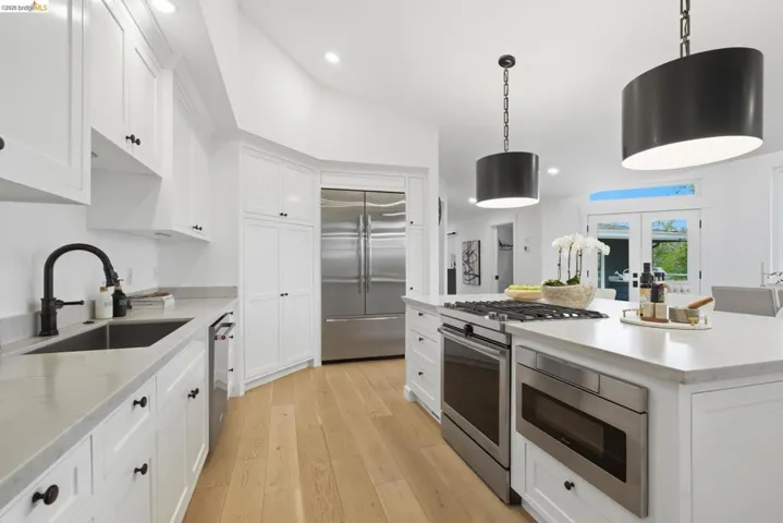 Modern kitchen featuring white cabinetry, light-toned wood-finish flooring, stainless steel appliances, and two pendant light fixtures