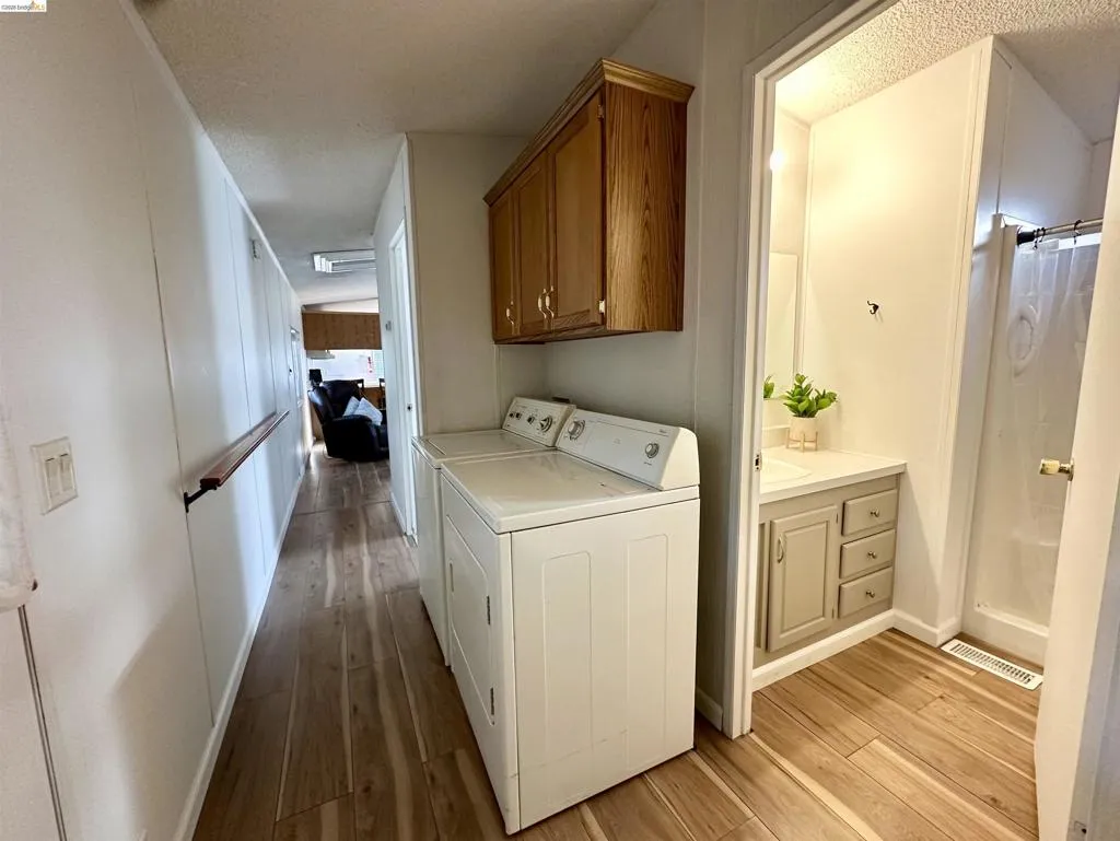 Laundry room featuring light wood finished floors, washing machine and clothes dryer, cabinet space, and a textured ceiling Laundry room featuring light wood finished floors, washing machine and clothes dryer, cabinet space, and a textured ceiling