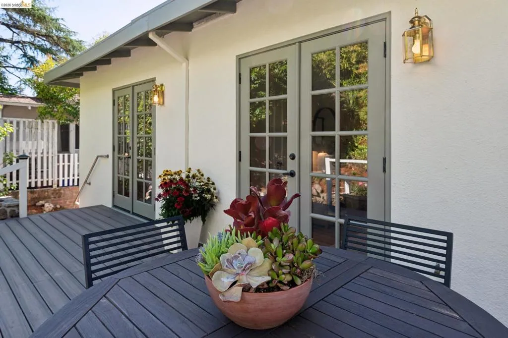 Expansive outdoor decking, multiple French doors with divided lites, wall-mounted exterior lighting, and a white picket fence Expansive outdoor decking, multiple French doors with divided lites, wall-mounted exterior lighting, and a white picket fence