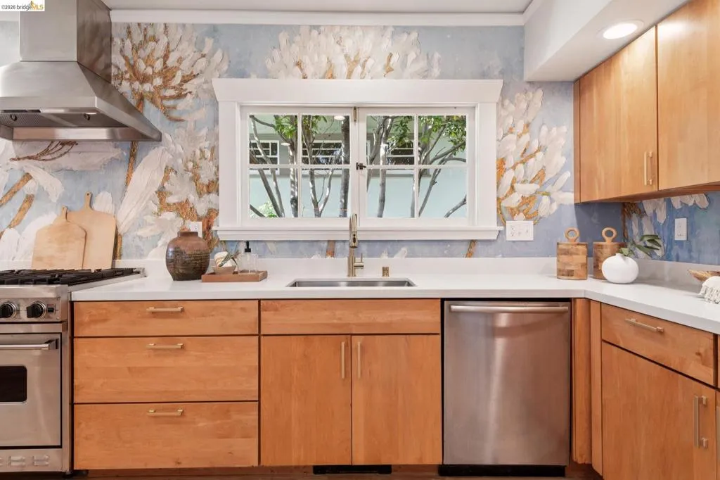 Wood-finish cabinetry with brass hardware, stainless steel appliances, a stainless steel range hood, white countertops, and a single-basin sink Wood-finish cabinetry with brass hardware, stainless steel appliances, a stainless steel range hood, white countertops, and a single-basin sink