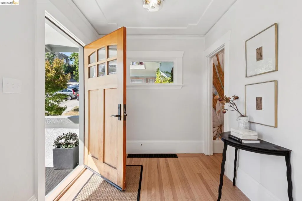 Entryway featuring a natural wood-finish door with glass panes, wood-finish flooring, a decorative ceiling light fixture, and a transom window Entryway featuring a natural wood-finish door with glass panes, wood-finish flooring, a decorative ceiling light fixture, and a transom window