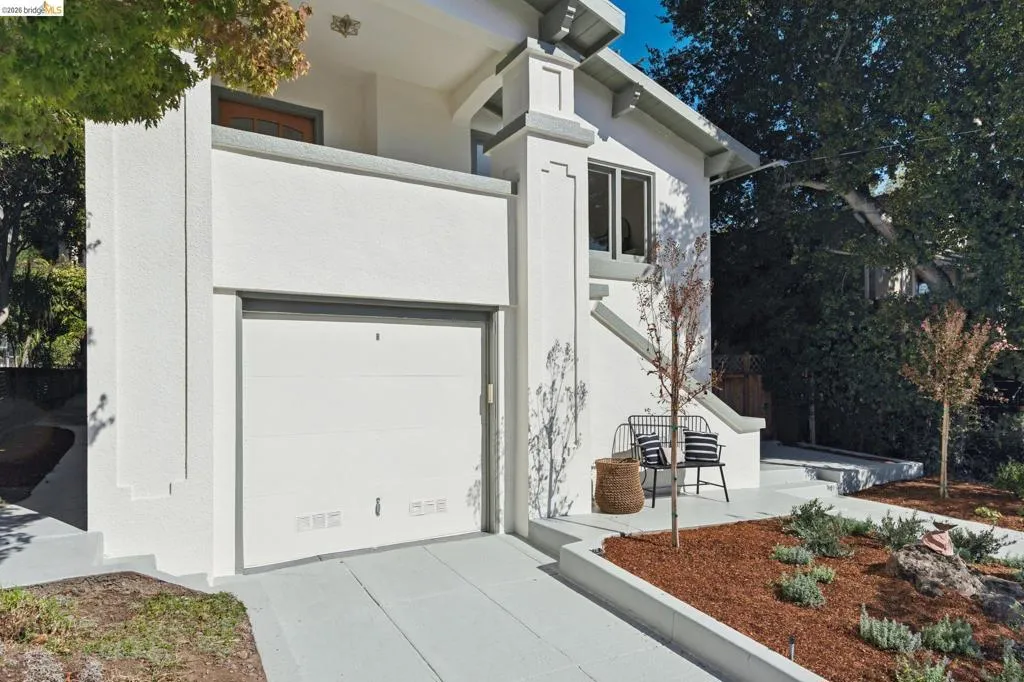 White stucco exterior with a garage, concrete driveway, front porch, mature trees, and landscaped garden beds White stucco exterior with a garage, concrete driveway, front porch, mature trees, and landscaped garden beds