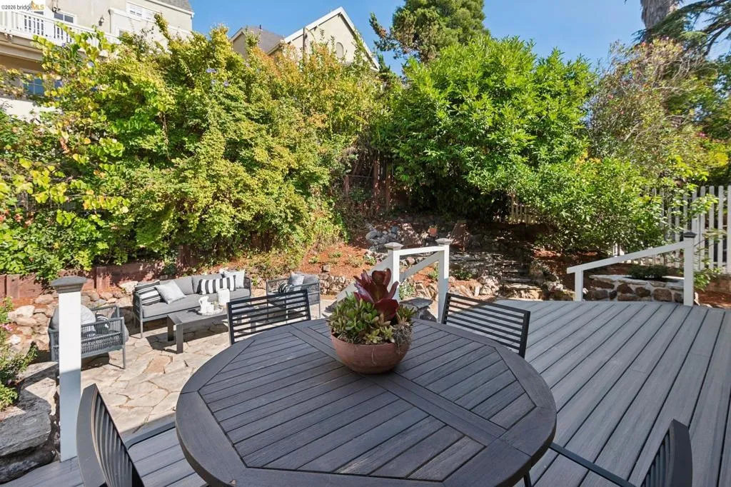 Expansive outdoor living area featuring a multi-level deck, stone patio, and natural landscaping with mature foliage Expansive outdoor living area featuring a multi-level deck, stone patio, and natural landscaping with mature foliage