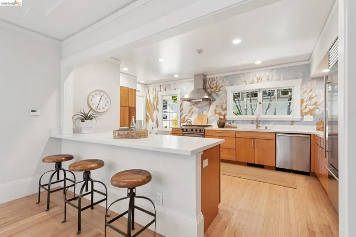 Kitchen featuring a breakfast bar, light wood cabinetry, stainless steel appliances, and a range hood
