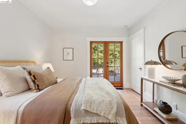 Double French doors with divided lites, light wood-finish flooring, white walls, and a built-in wall mirror