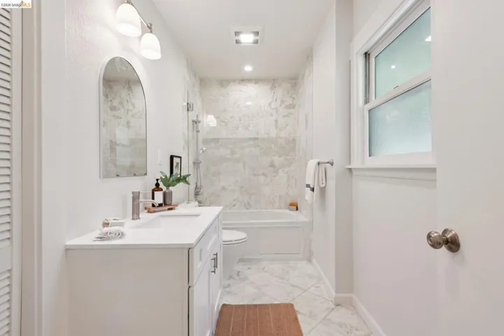 White vanity with a single basin, wall-mounted light fixture, and arched mirror