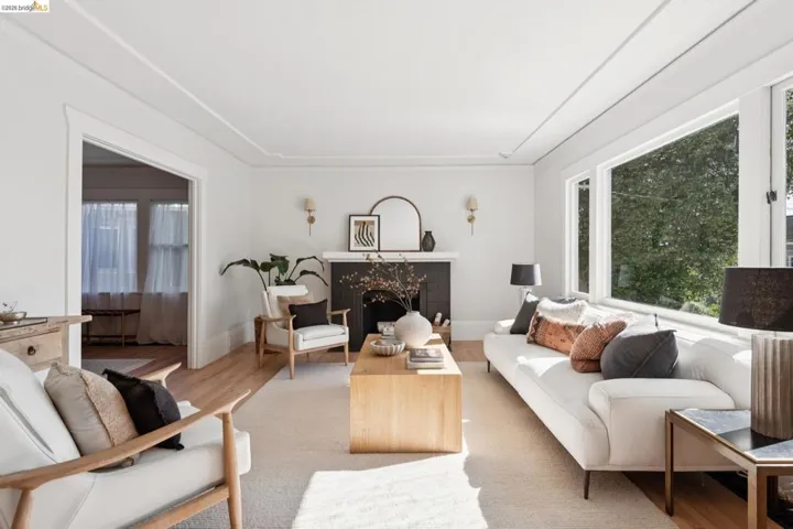 Spacious living area featuring large windows, wood-finish flooring, a fireplace with a dark-tiled surround, and decorative ceiling trim