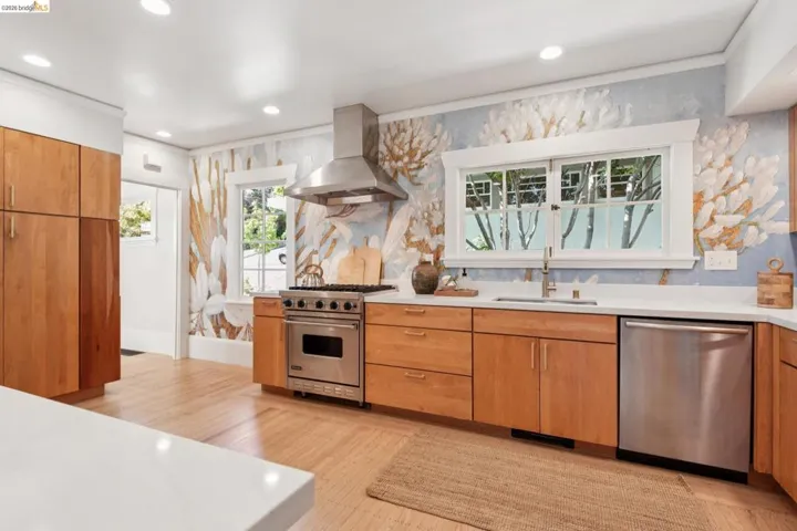 Stainless steel appliances, light wood-finish cabinetry, white countertops, recessed lighting, and light wood-finish flooring