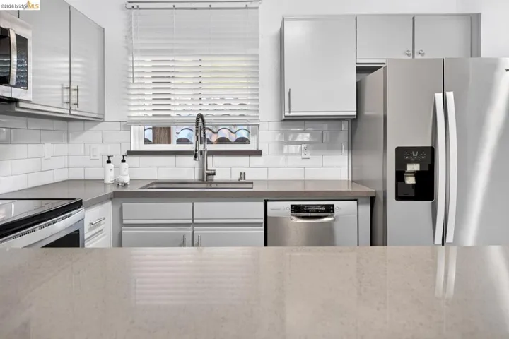 Stainless steel appliances, white subway tile backsplash, light-toned countertops, and light gray cabinetry