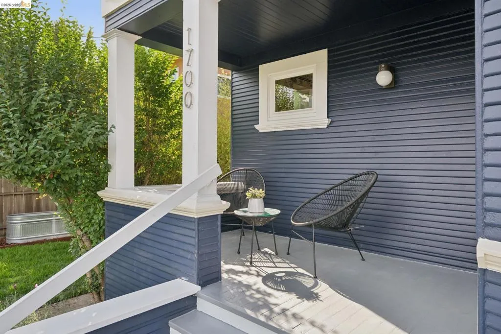 Painted wood siding with contrasting trim, covered front porch, white painted columns, exterior wall-mounted light fixture, and address numbers