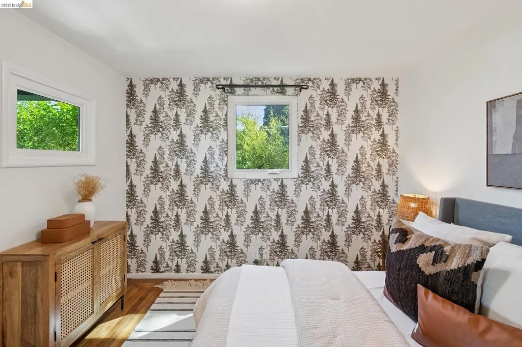 Hardwood flooring, white painted walls, patterned accent wall, and multiple windows with white trim