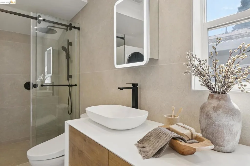 Contemporary bathroom featuring a floating wood-finish vanity with a vessel sink, a matte black faucet, and a frameless glass shower enclosure with a rain showerhead