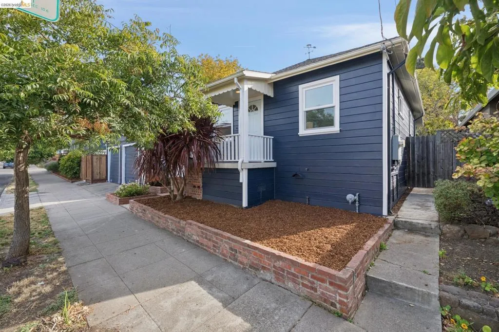 Exterior featuring blue horizontal siding, a covered porch with white railings, a brick-edged planting bed, a concrete sidewalk, and a side walkway