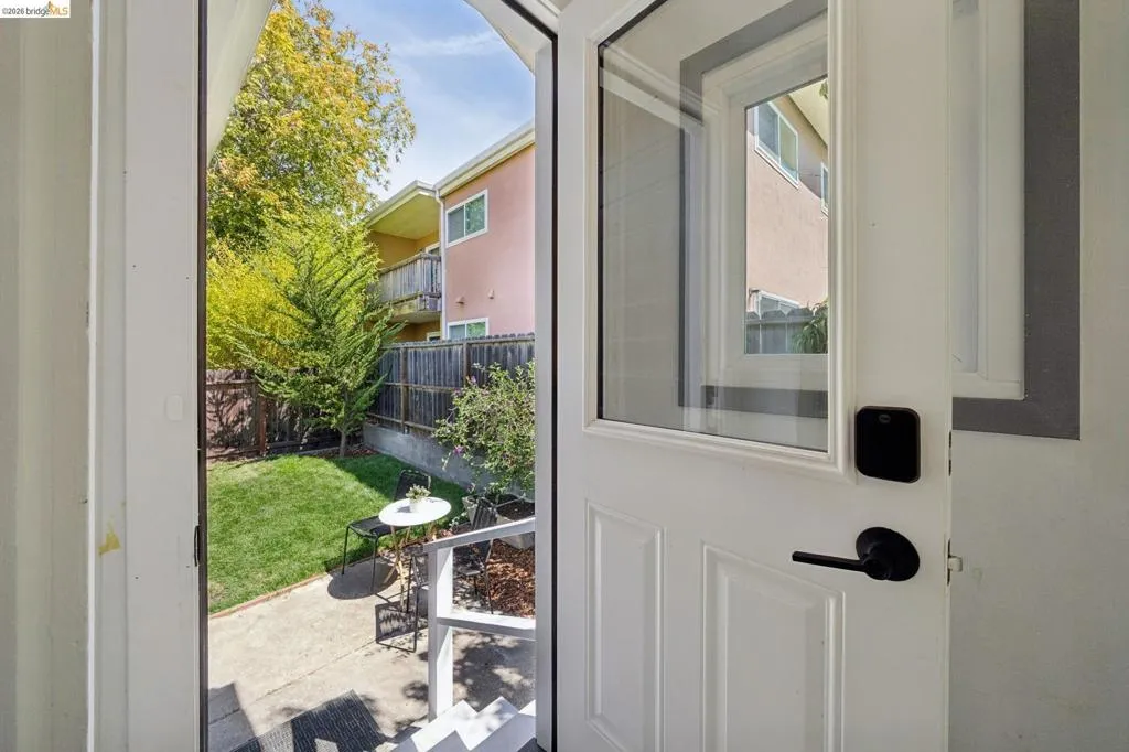 White entry door with a rectangular window panel and matte black hardware, opening to a private outdoor space