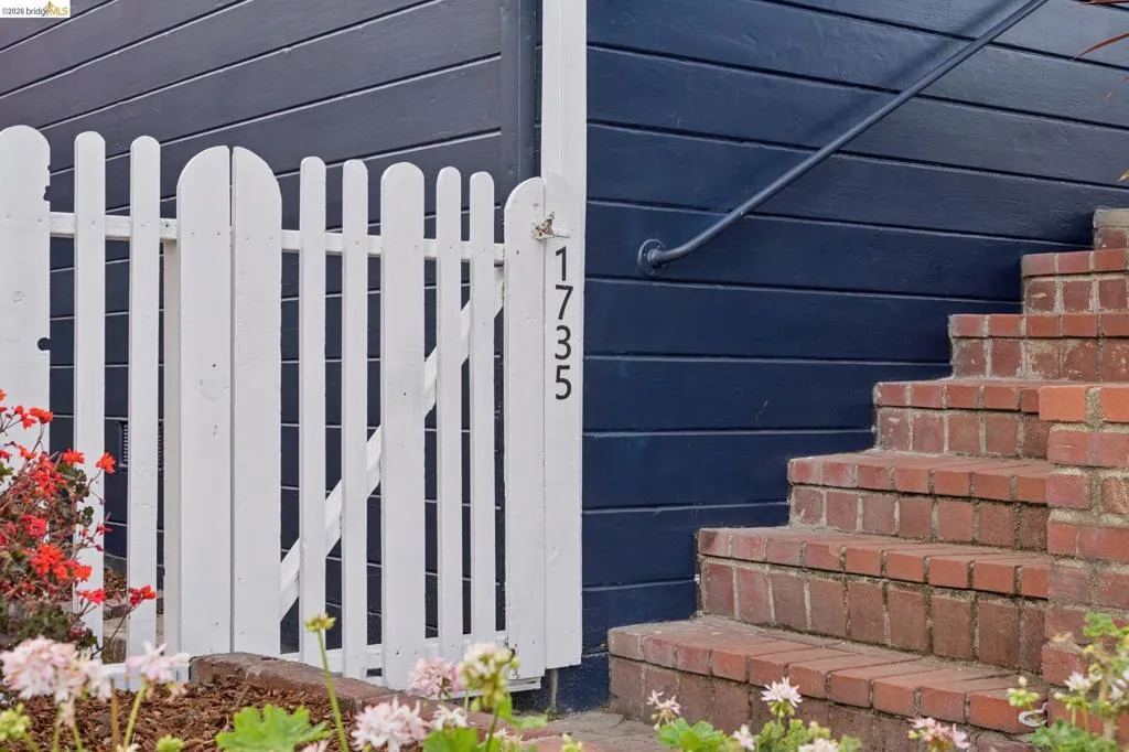 White picket gate, dark-toned horizontal siding, brick-laid stairs, and a dark metal handrail