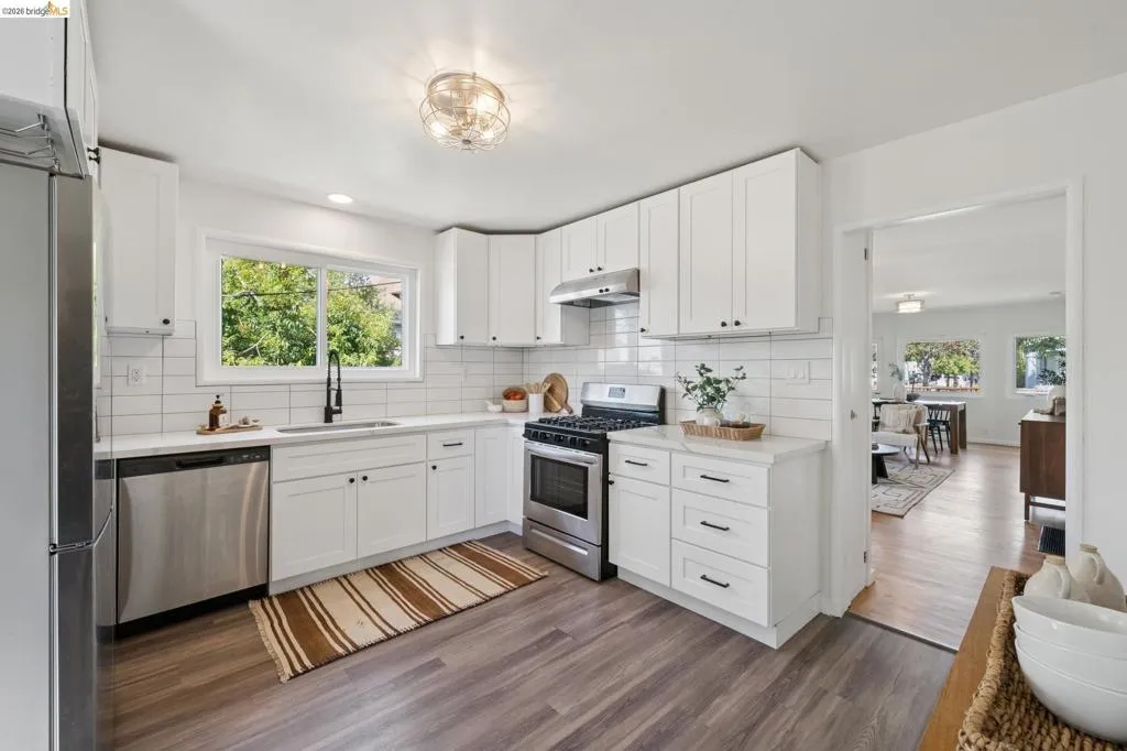 White shaker-style cabinetry with matte black hardware, stainless steel appliances, a subway tile backsplash, and a large kitchen window
