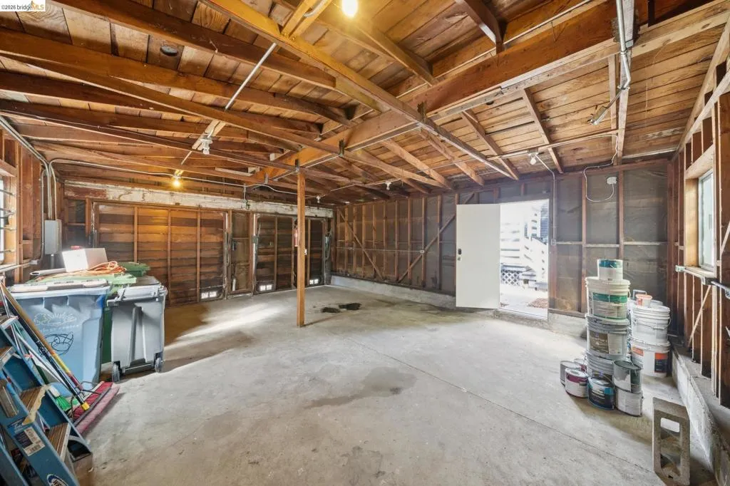 Exposed wood beam ceiling, raw wood wall framing, concrete flooring, exterior-facing window, and an exterior door
