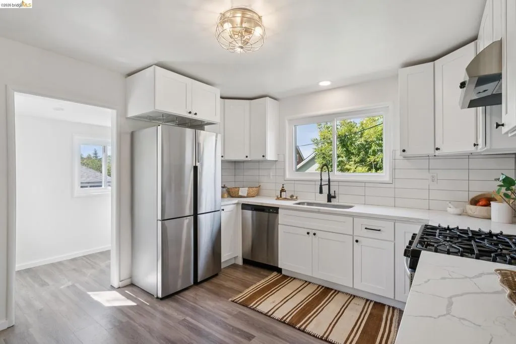 Modern kitchen featuring white shaker-style cabinetry, white subway tile backsplash, light-toned countertops, and wood-finish flooring