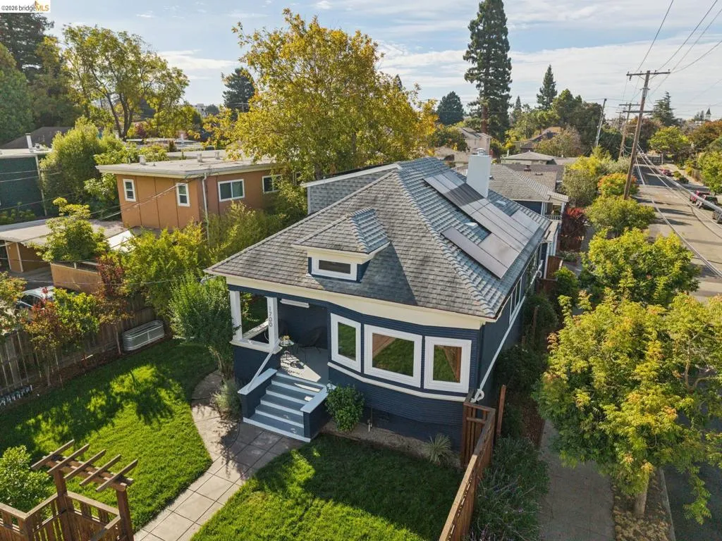 Gable roofline with dormer, solar panel array, bay window, front porch with steps, and a fenced yard with established landscaping