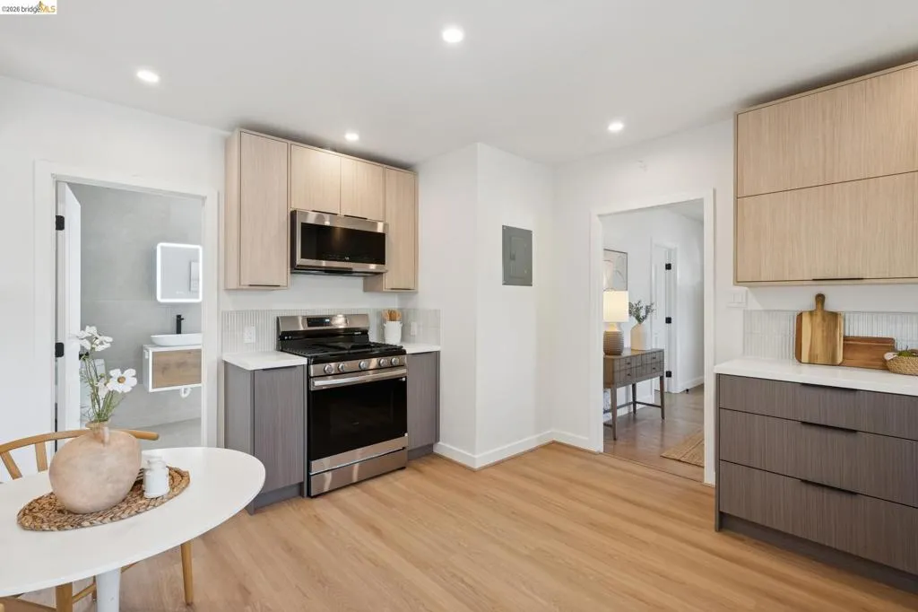 Kitchen featuring wood-finish flooring, two-tone cabinetry, stainless steel appliances, a white tile backsplash, and recessed lighting