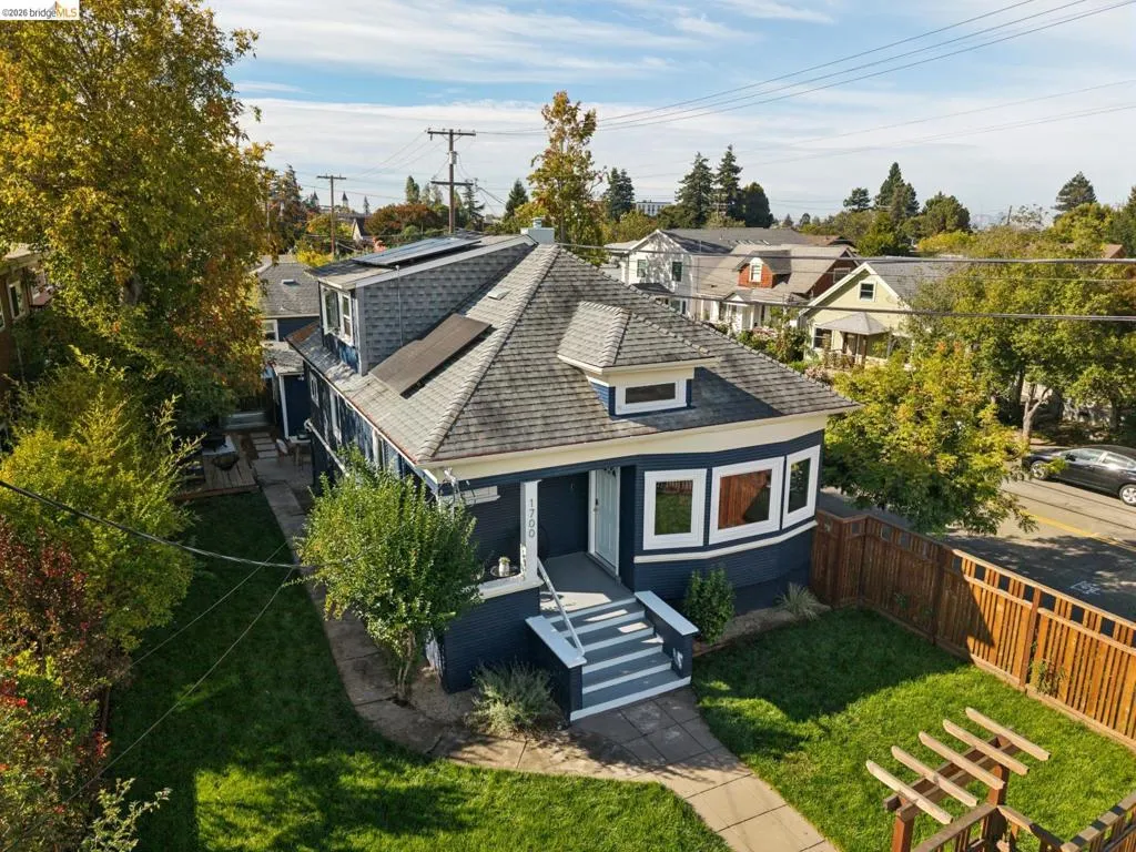 Shingled roof with solar panels, bay window, exterior steps, and a fenced yard with a privacy fence
