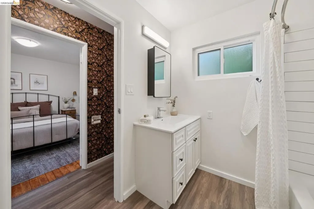 White vanity with integrated sink, wood-finish flooring, a white window, and a shower with horizontal paneling