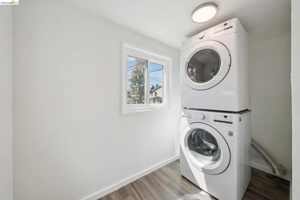 Laundry area featuring a stackable washer and dryer, wood-finish flooring, a window, and overhead lighting