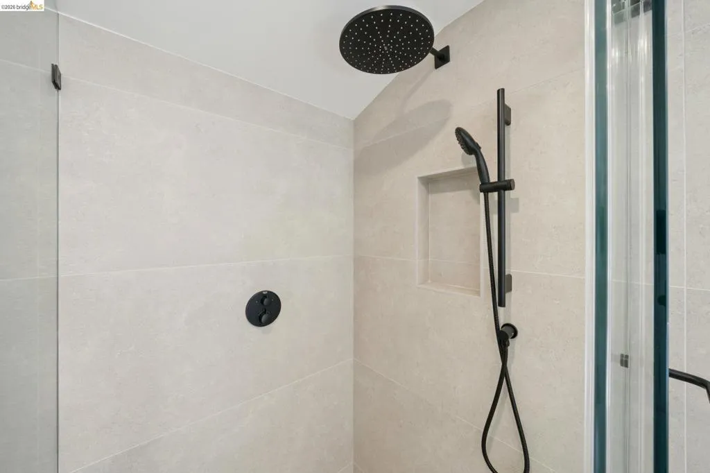 Shower with light-toned tiled walls, matte black fixtures, rain shower head, and an integrated niche