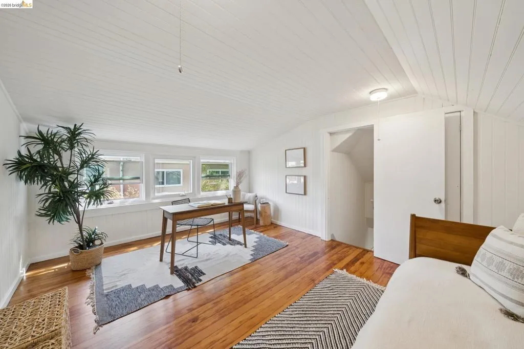 Hardwood flooring, multiple windows, beadboard ceiling, white wall paneling, and a flush mount light fixture