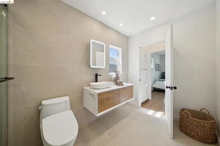Floating vanity with wood-finish drawer fronts, vessel sink, matte black faucet, and illuminated mirror