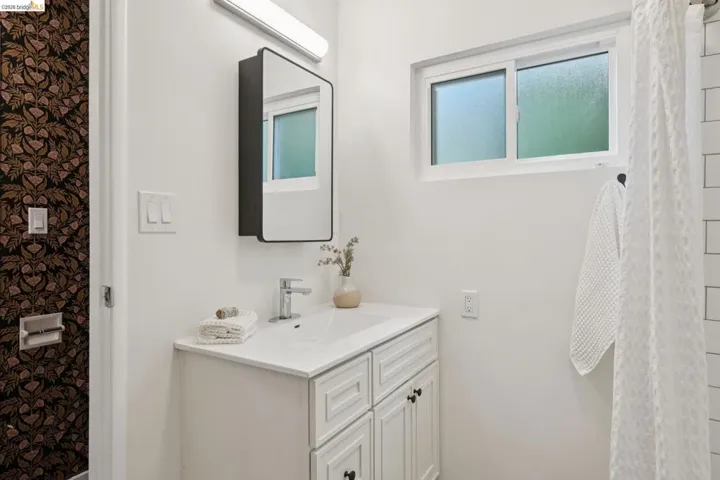 White shaker-style vanity with integrated sink, chrome-finish faucet, and a rectangular mirrored medicine cabinet