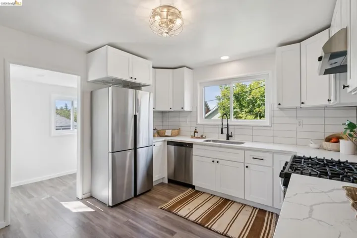 Modern kitchen featuring white shaker-style cabinetry, white subway tile backsplash, light-toned countertops, and wood-finish flooring