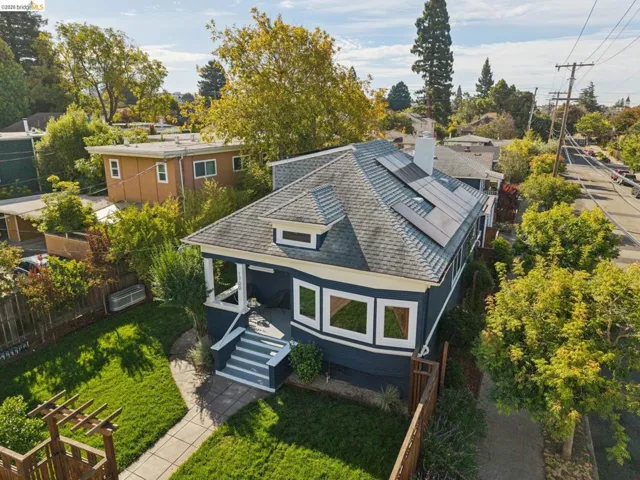 Gable roofline with dormer, solar panel array, bay window, front porch with steps, and a fenced yard with established landscaping