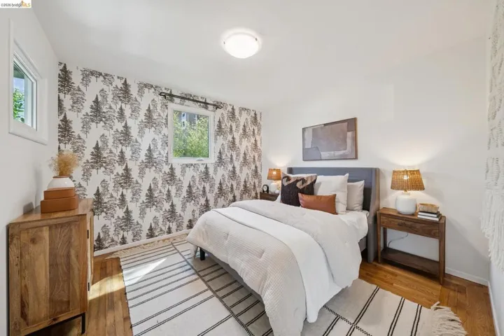 Hardwood-finish flooring, accent wall with botanical pattern, window with white trim, built-in ceiling light, white wall finishes